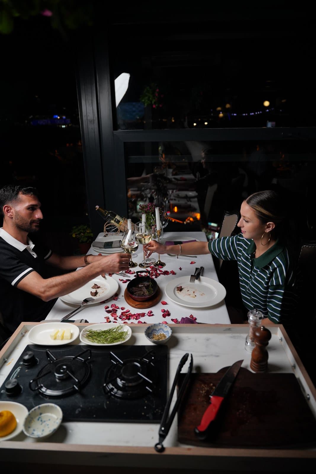 Two guests toasting with white wine at an evening table on the Pino Gare terrace