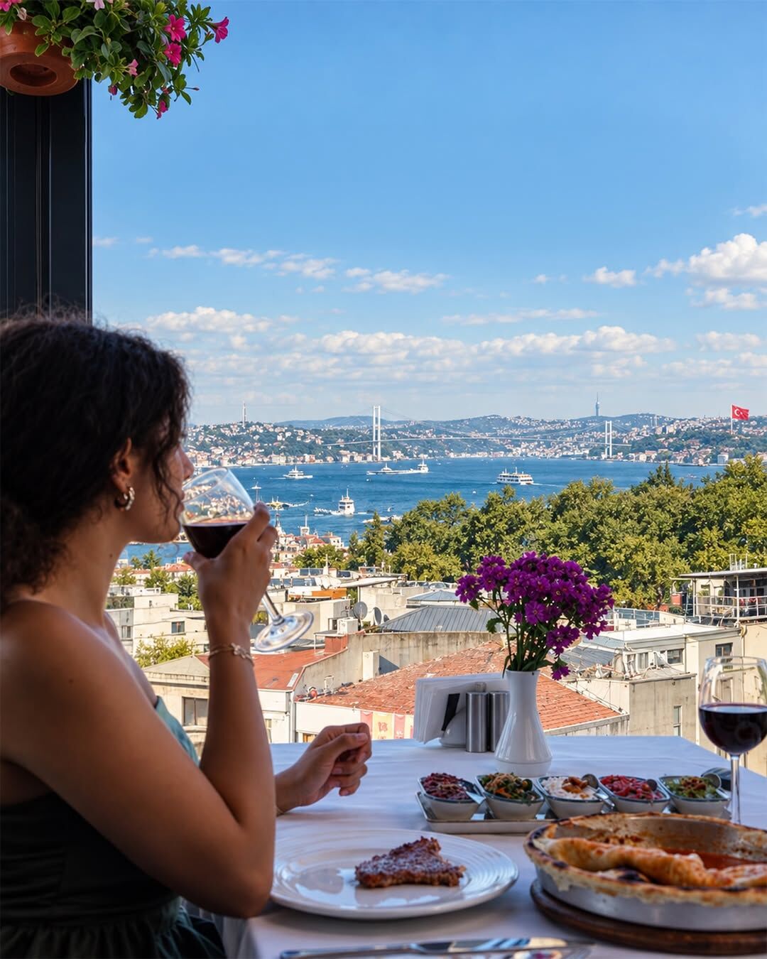 Red wine at a Pino Gare terrace table set with meze and pide, the Bosphorus and its bridge behind